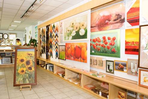 Wand mit Kunstdrucken, unter anderem Mohnblumen- und Tulpenmotiven, im Verkaufsraum